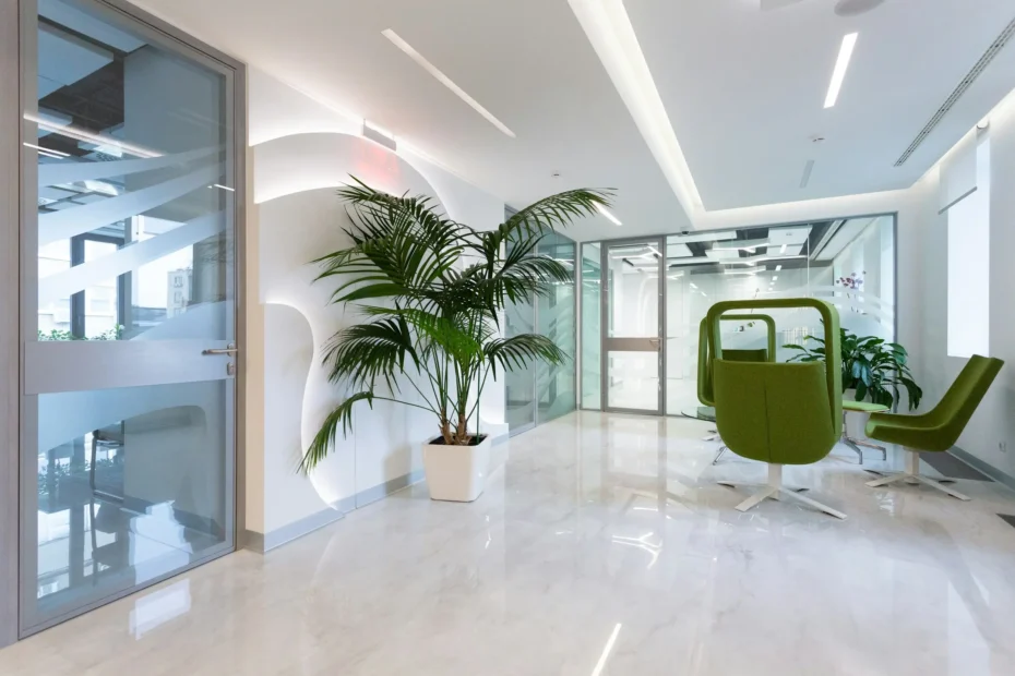 A bright, modern office lobby with a potted palm, glass walls, and green accent chairs