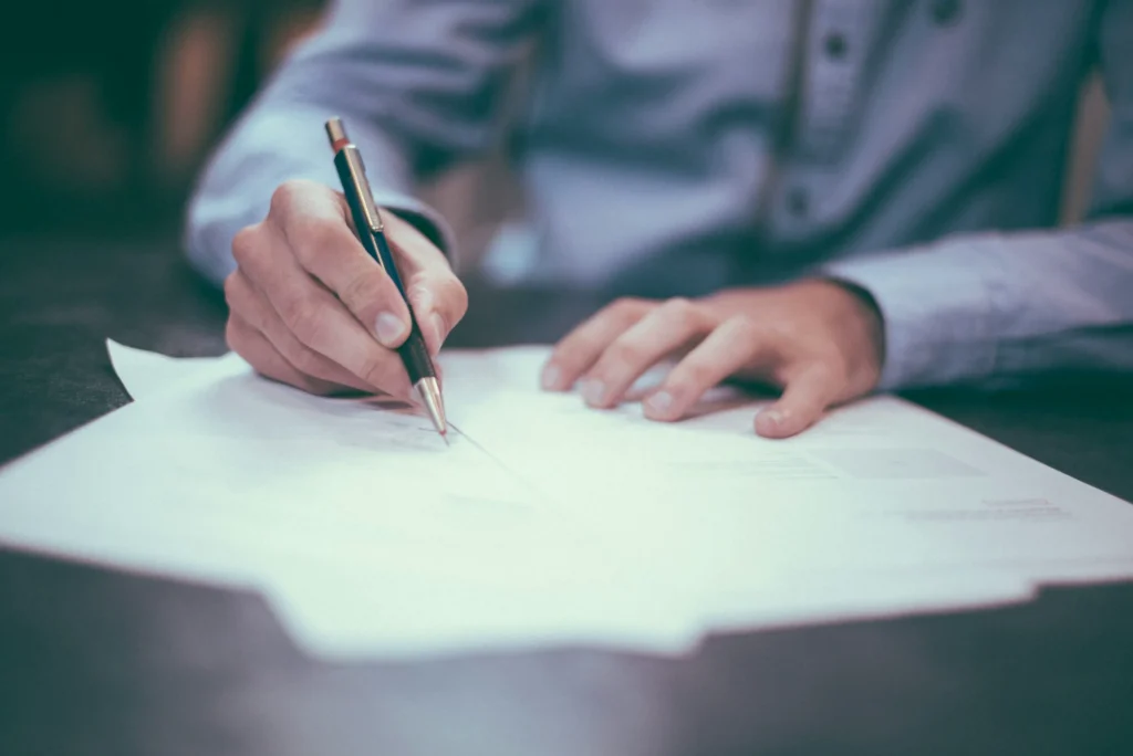 Close-up of a hand signing a paper contract at a desk.