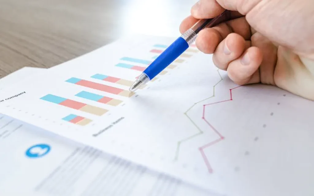 A hand pointing a pen at colourful bar and line charts on paper
