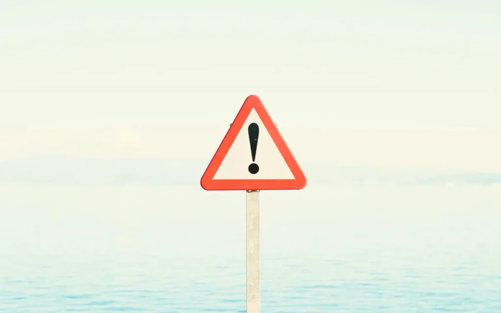 Red warning triangle on a pole against a calm pale sea