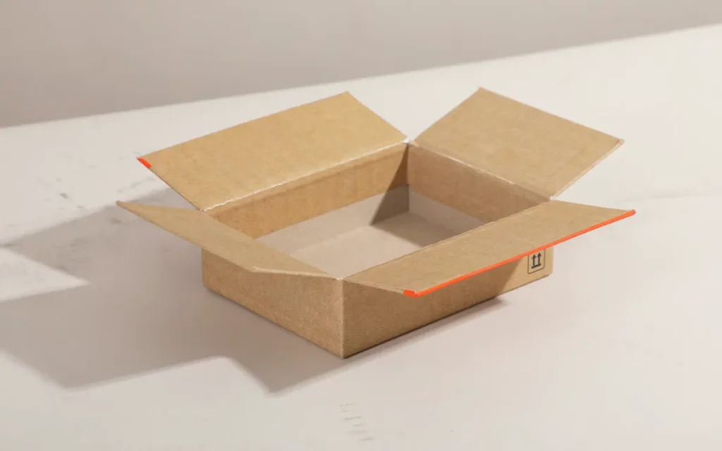 Open kraft cardboard box with its flaps spread on a pale table