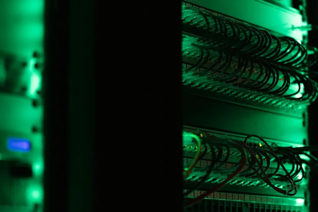 Network cables connected to a server rack, lit green in a dark room