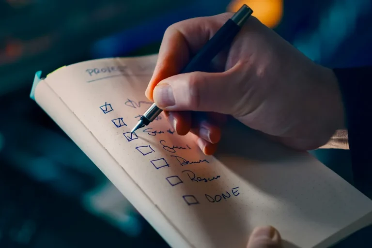 A hand ticking items off a handwritten checklist in a notebook