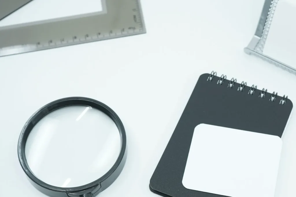 A magnifying glass and a closed spiral notebook on a white desk